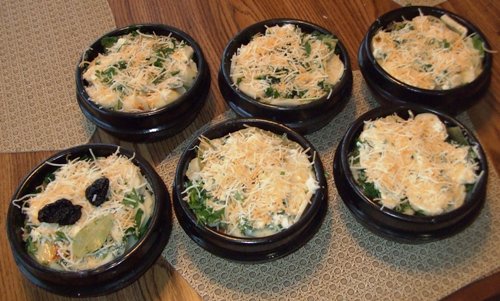 Top view of six chicken clay pot with shredded cheese.