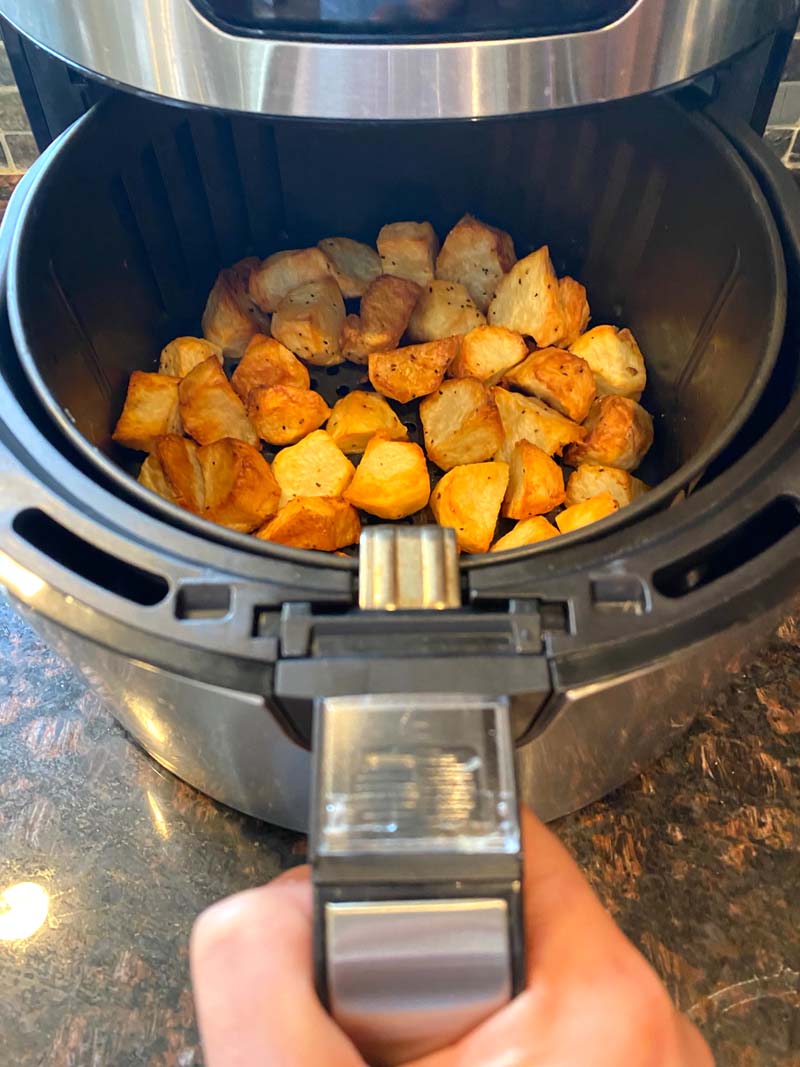 The potatoes being pulled out of the air fryer to serve