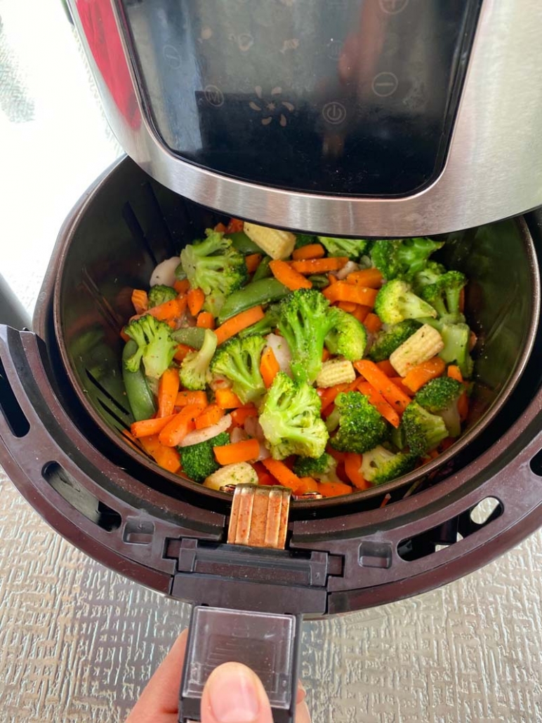 Pulling out the basket from the air fryer with mixed vegetables inside 