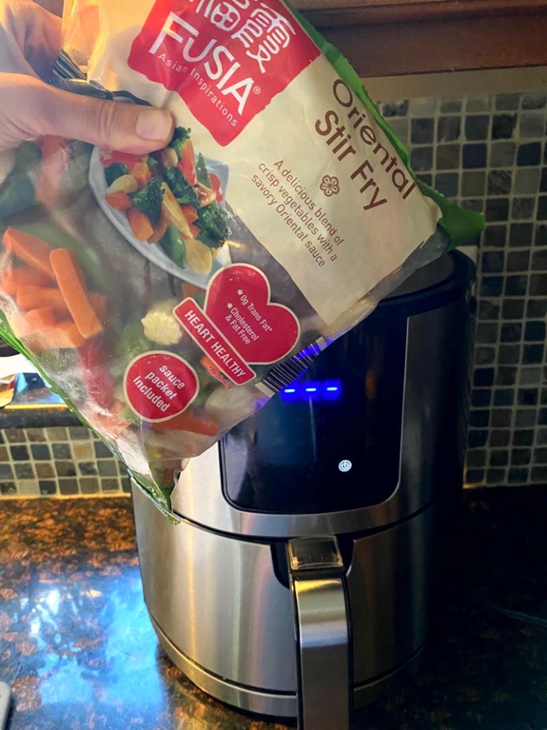 A bag of oriental stir fry mixed vegetables being held in front of an air fryer 