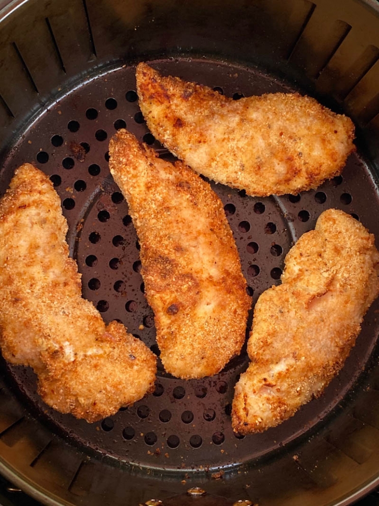 breaded chicken tenderloins in an air fryer basket 