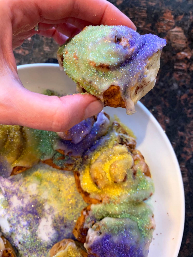 hand holding a cinnamon roll turned king cake for mardi gras 