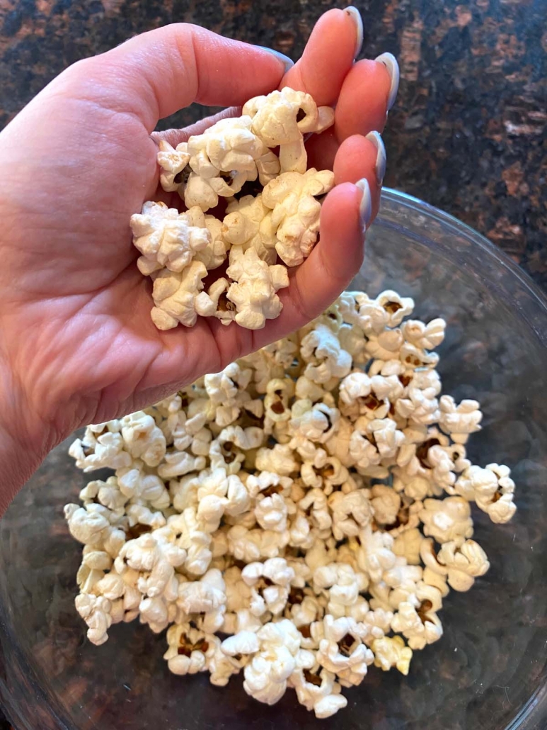 hand holding popcorn above bowl of popcorn