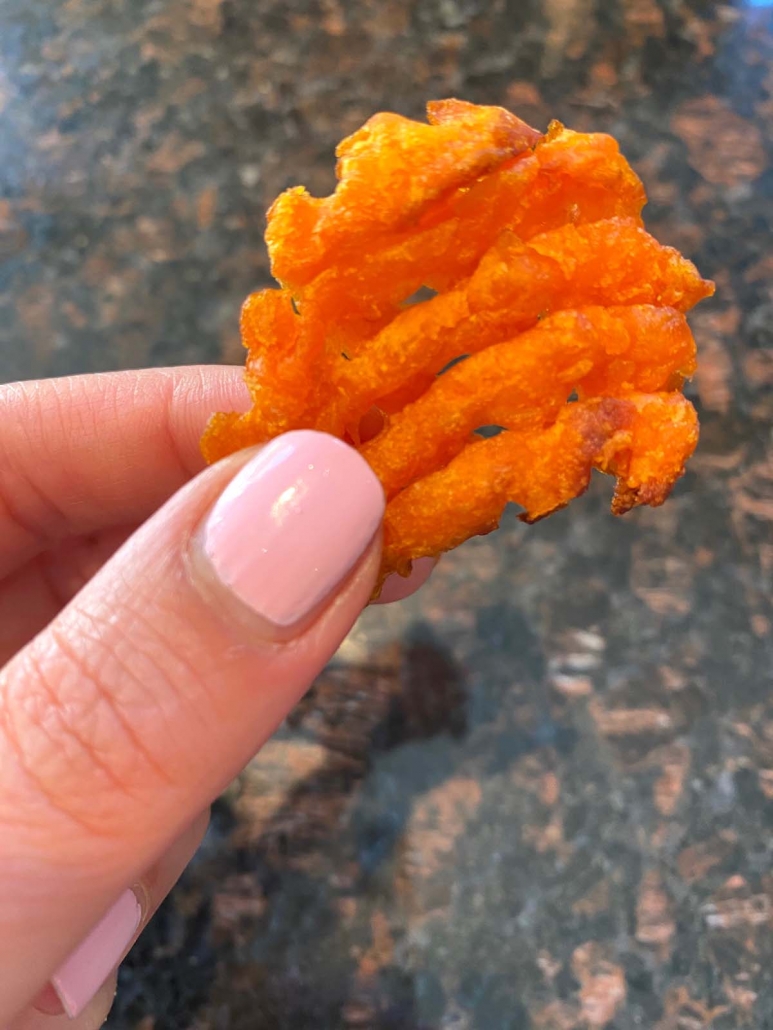 hand holding single sweet potato waffle fry