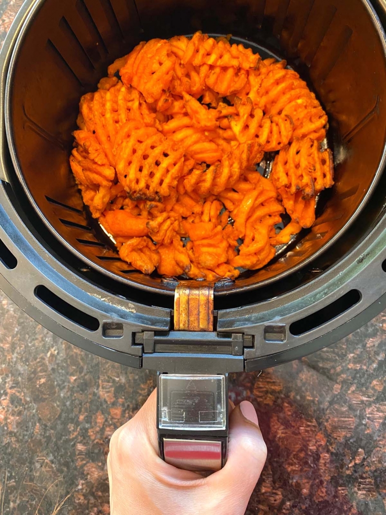 hand holding air fryer with sweet potato waffle fries