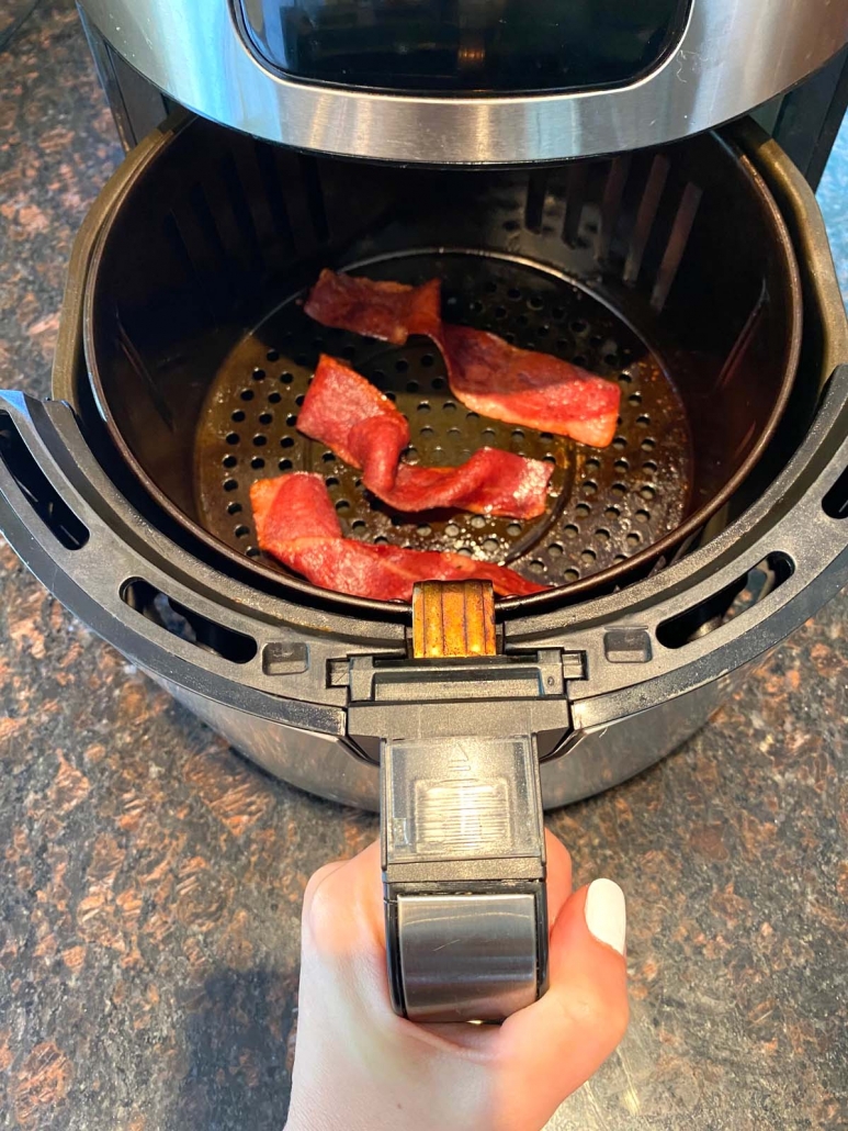 hand holding air fryer basket with turkey bacon inside