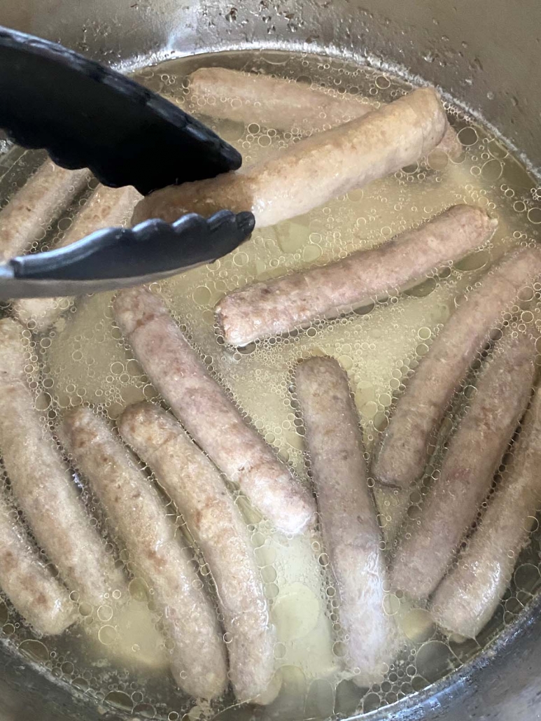 tongs holding sausage link above instant pot