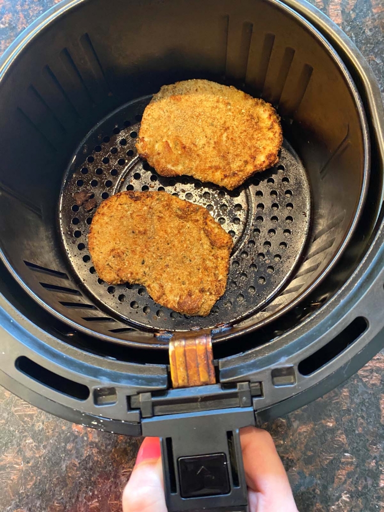 two breaded chicken cutlets in the air fryer basket
