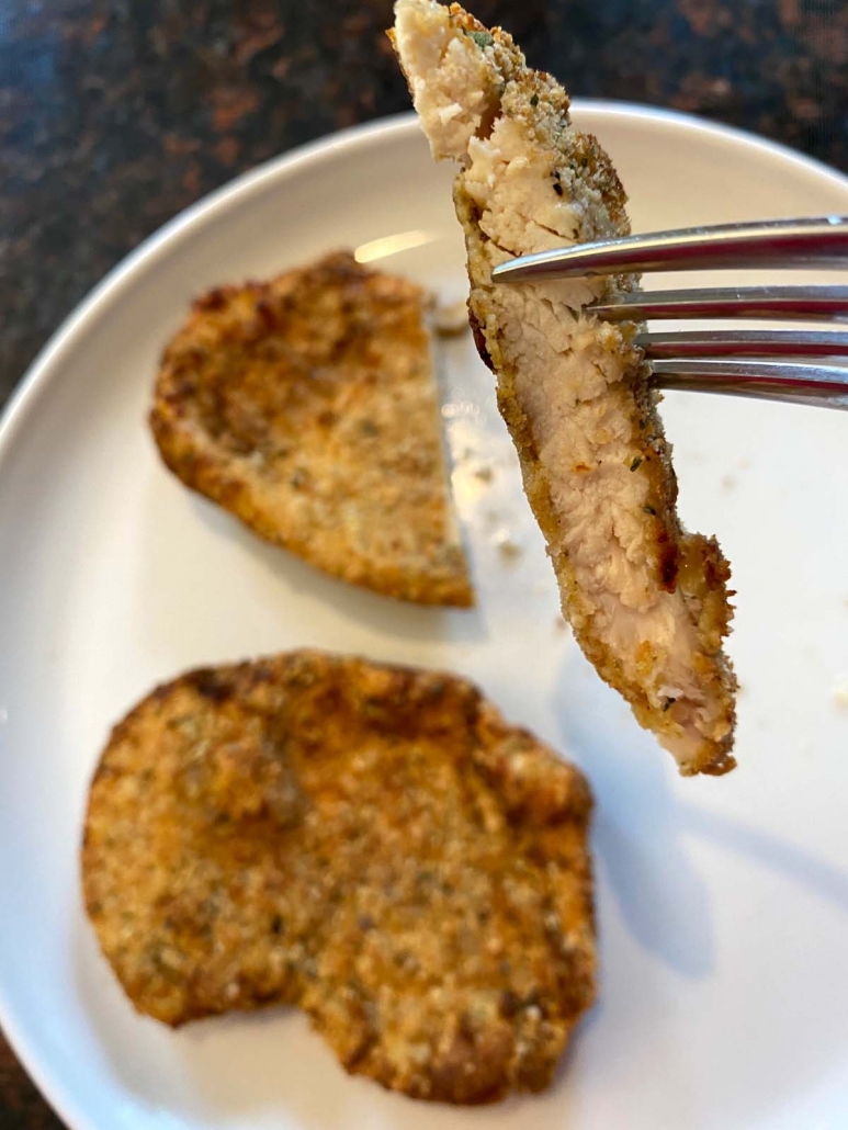 fork holding piece of chicken cutlet over plate of cutlets