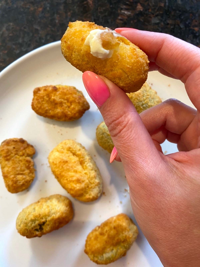 hand holding jalapeno popper over plate of poppers