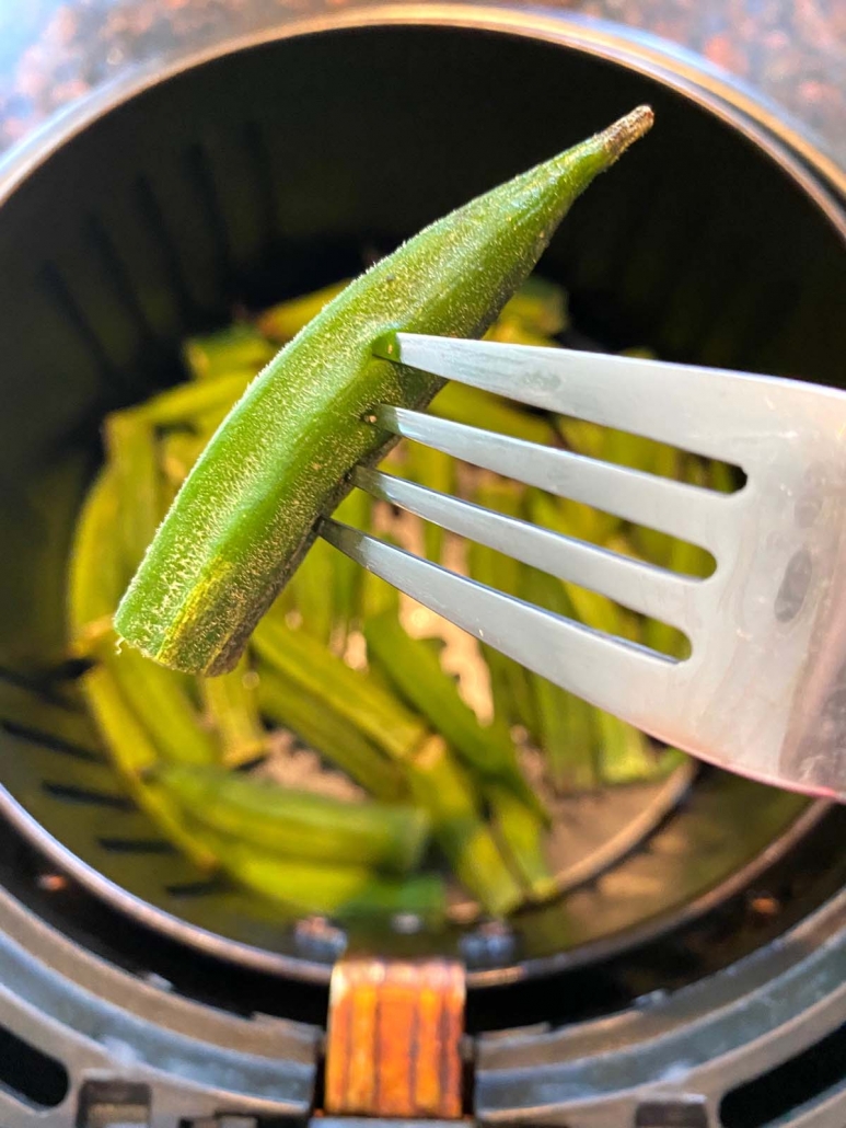 fork holding okra above air fryer