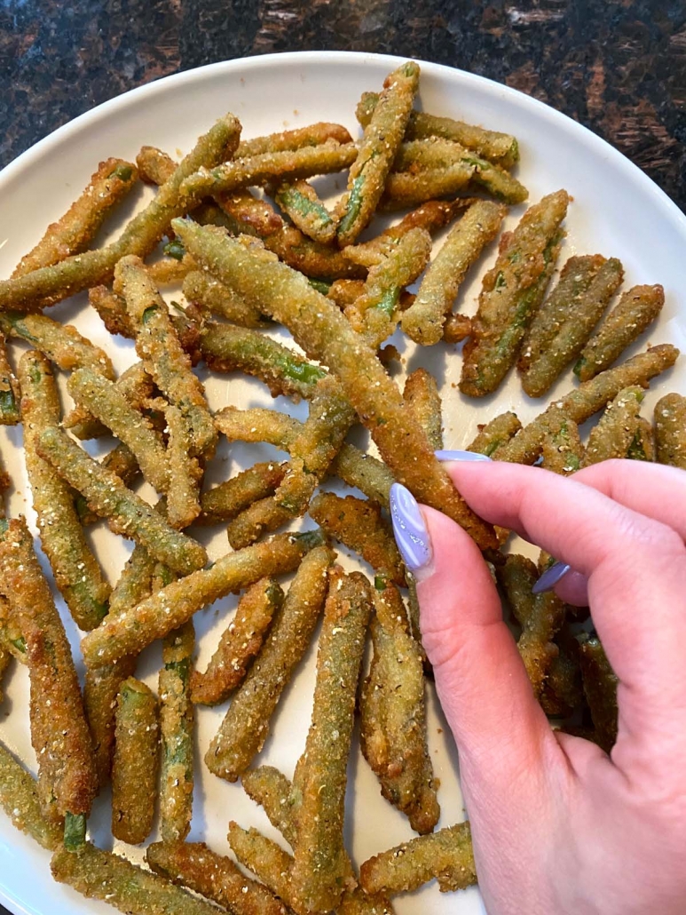 breaded green beans on plate with hand holding one green bean