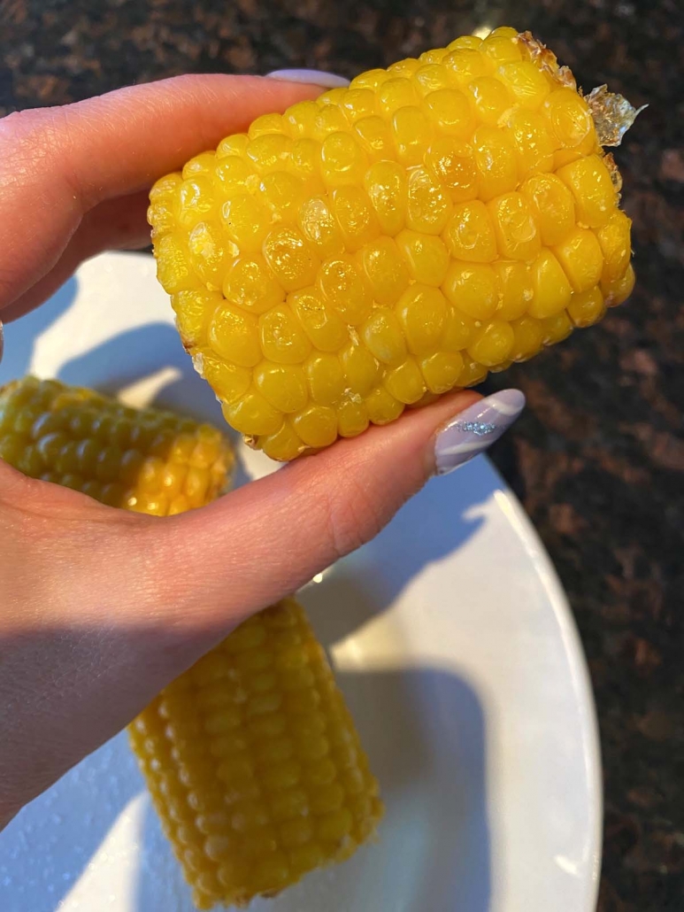 hand holding corn on the cob over plate