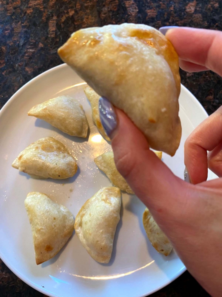 hand holding pierogi above plate with pierogies