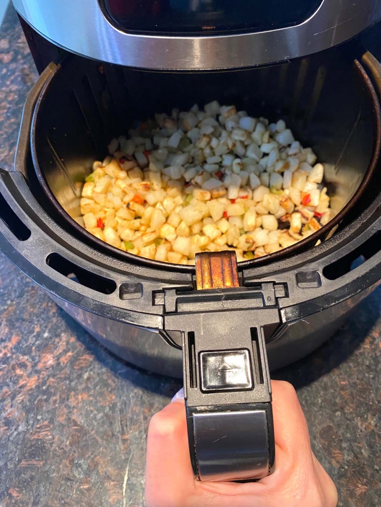 hand holding air fryer basket with diced potatoes inside