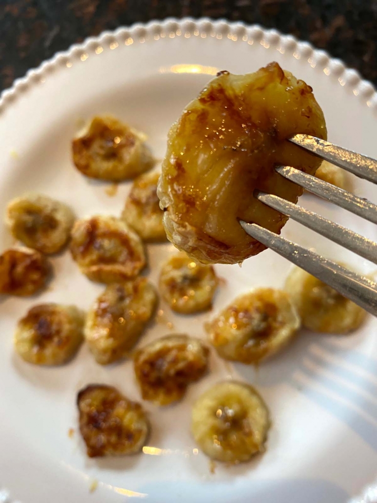 fork holding air fried banana slice above plate of banana slices