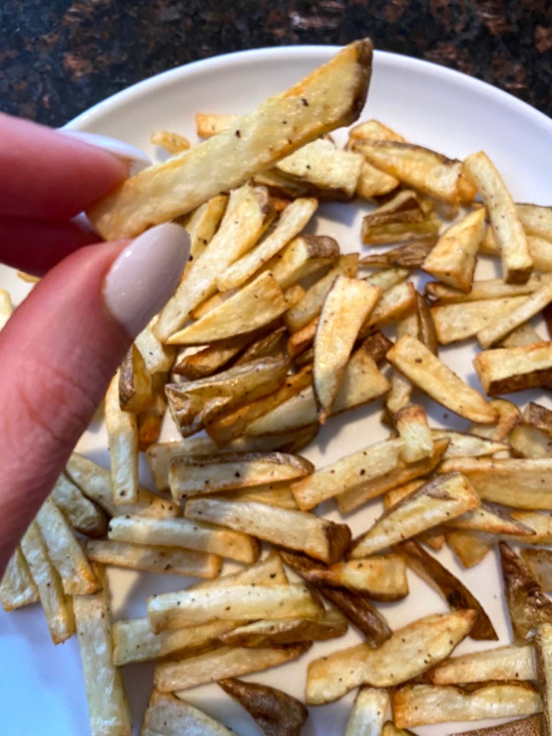 hand holding french fry over plate filled with fries