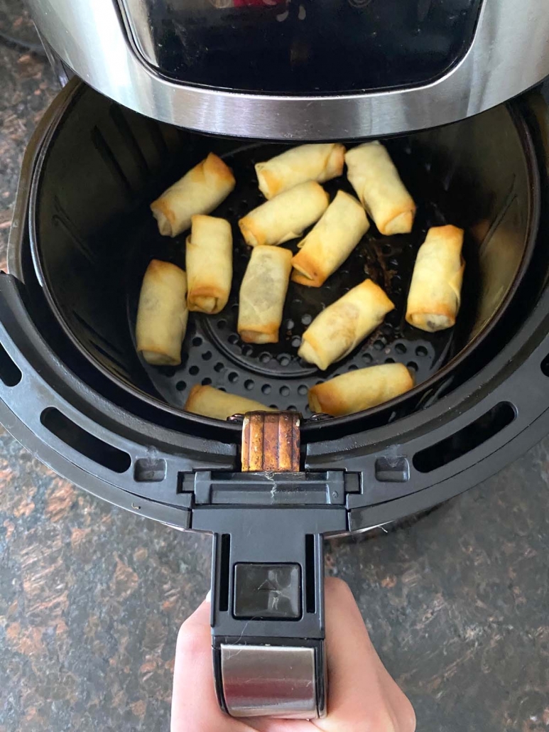 hand holding air fryer basket with frozen spring rolls inside