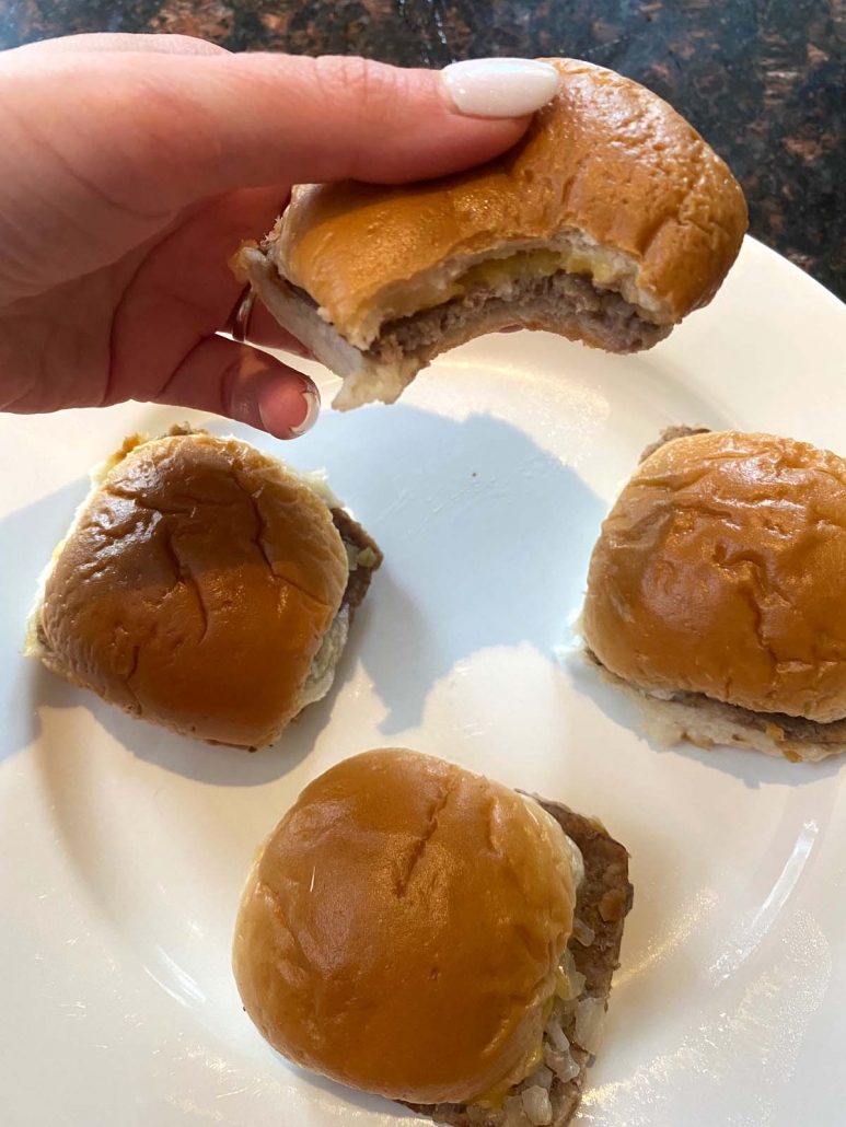 hand holding white castle slider above plate with other sliders