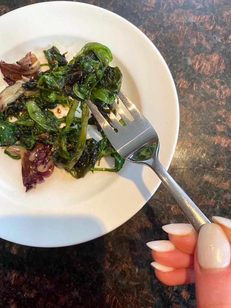 fork picking up sauteed lettuce from a plate