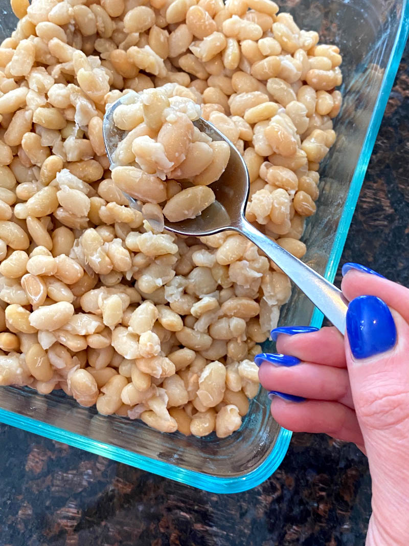 Cooked great northern beans in a dish with a spoon of them.