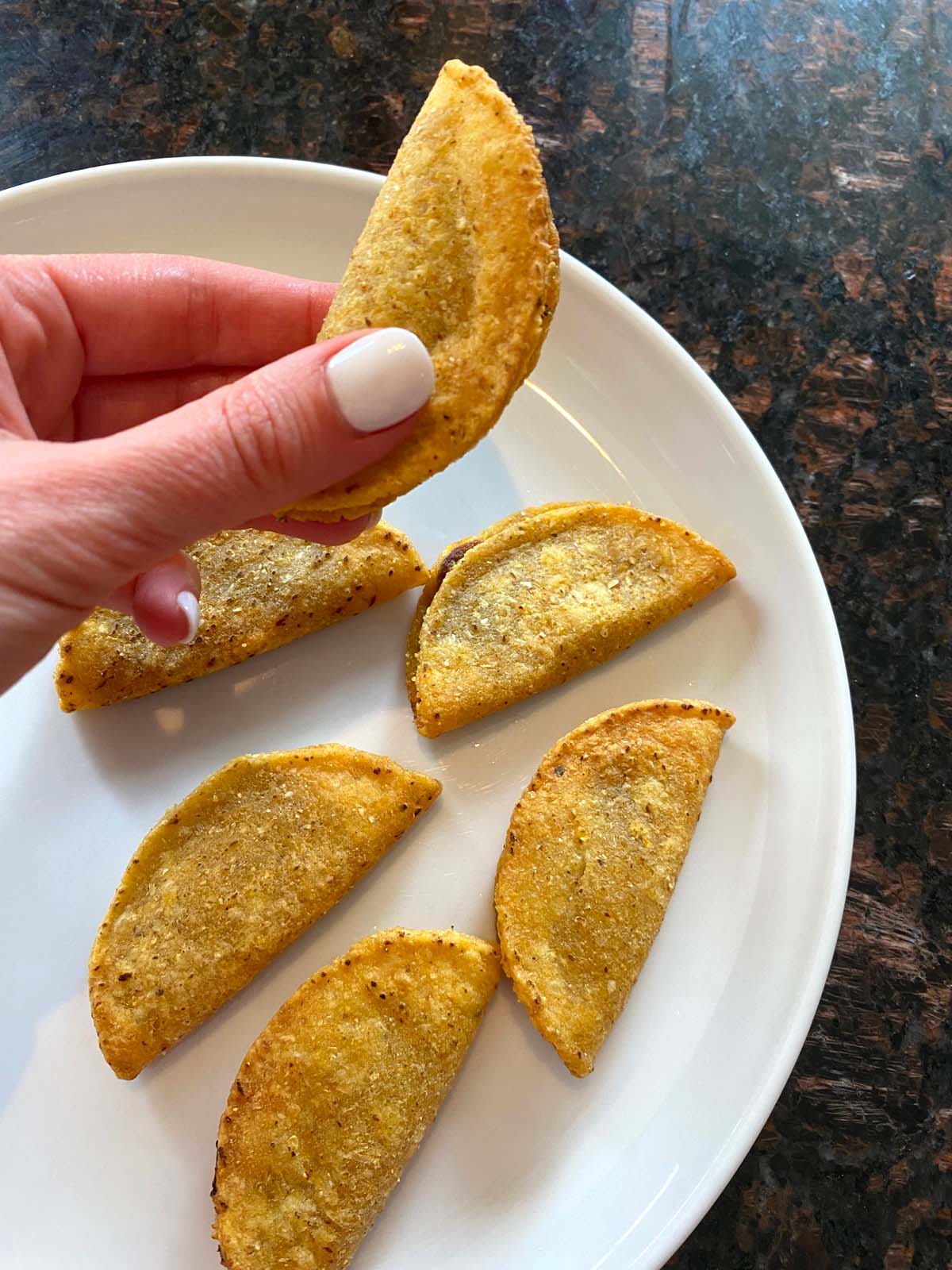 Hand holding a taco with more on a plate below.