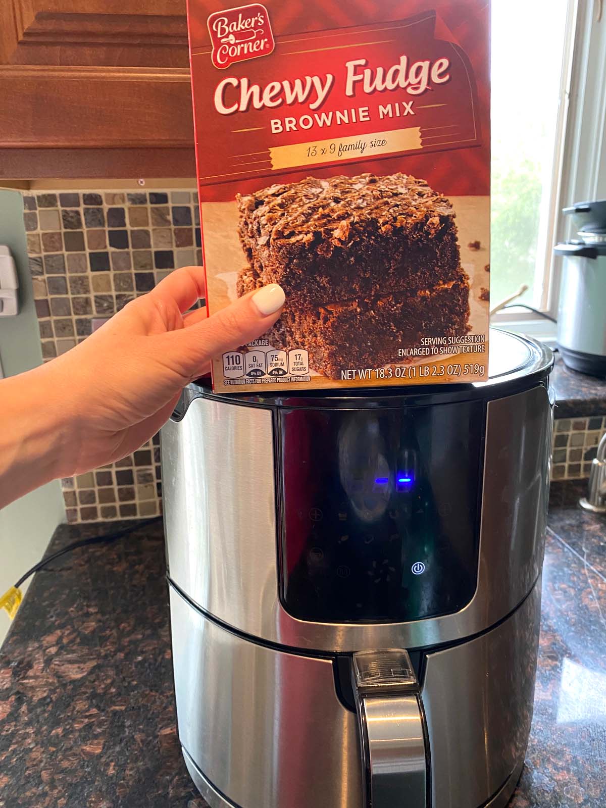 Box of brownie mix held in front of an air fryer.