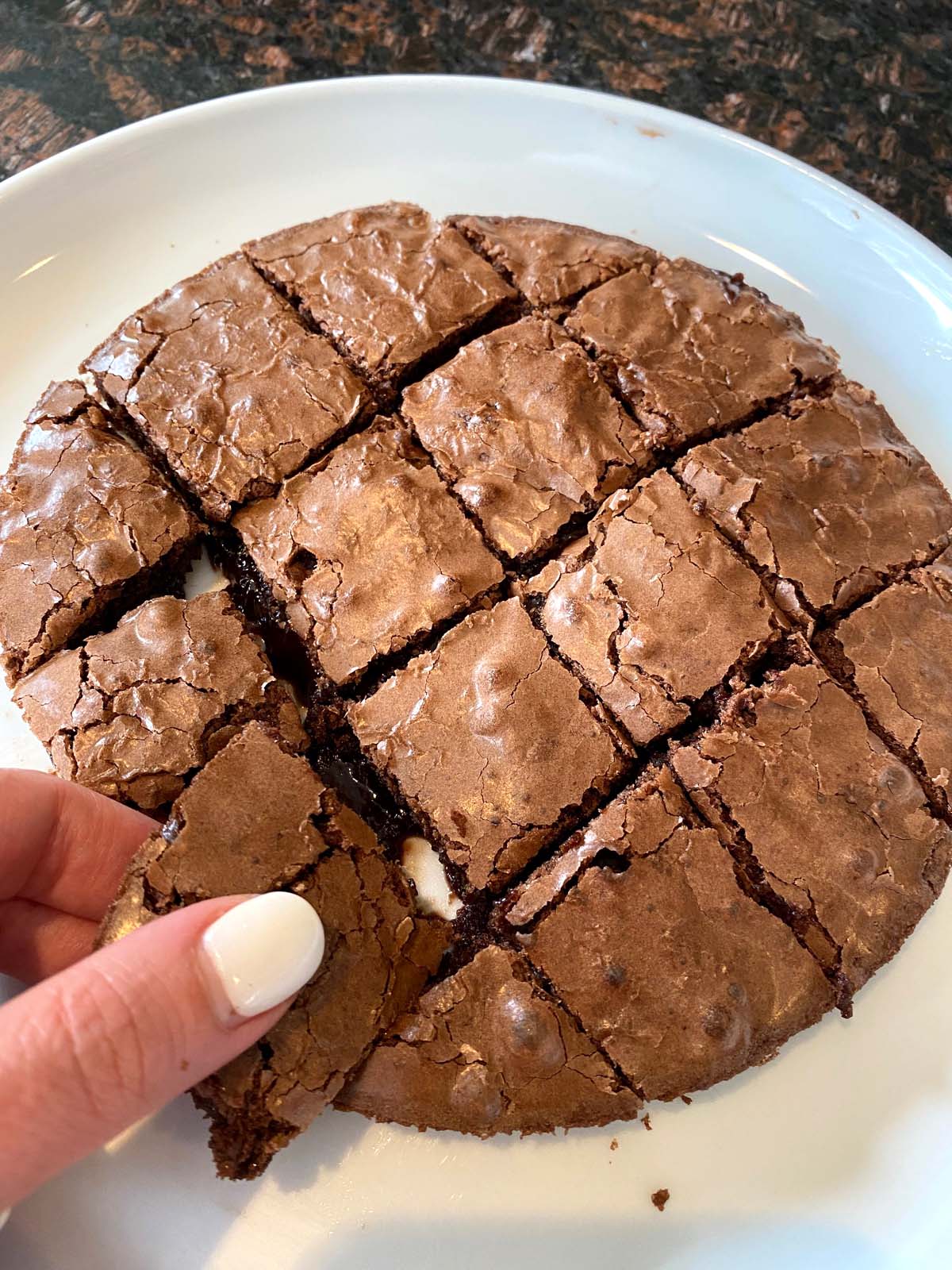 Hand picking up a piece of brownie from plate.