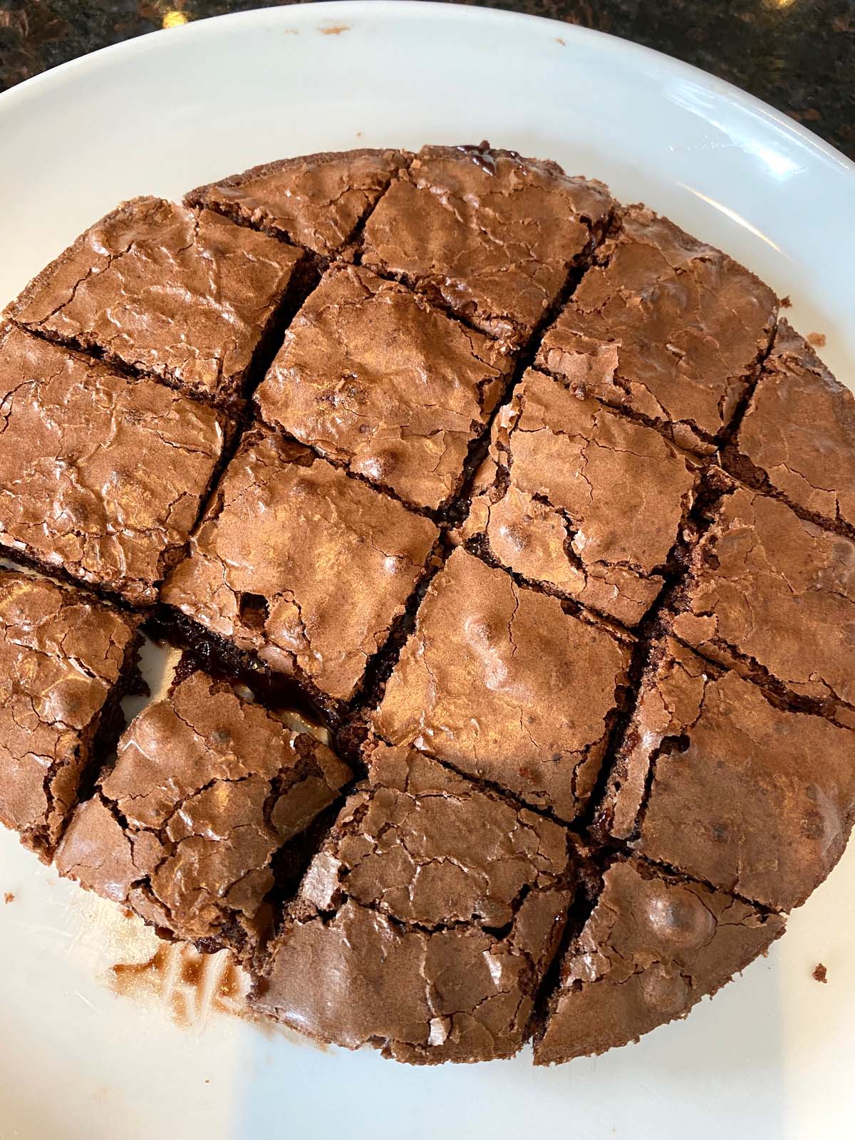 Close up of fudgy brownies cut into squares on a large round plate.
