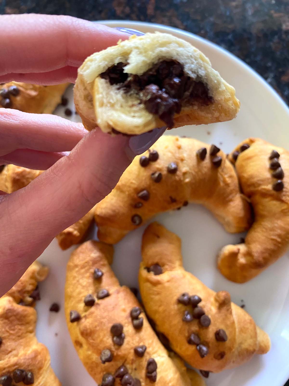 Chocolate croissants on a plate with one torn in half.