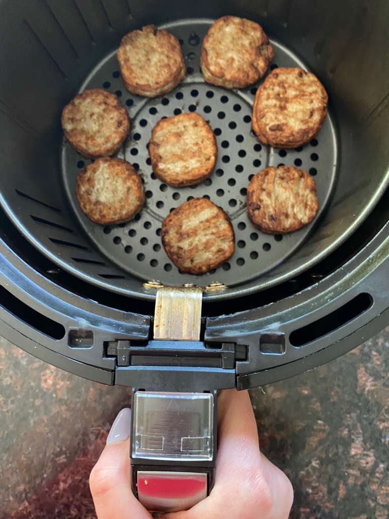 hand holding air fryer basket with breakfast sausage patties inside