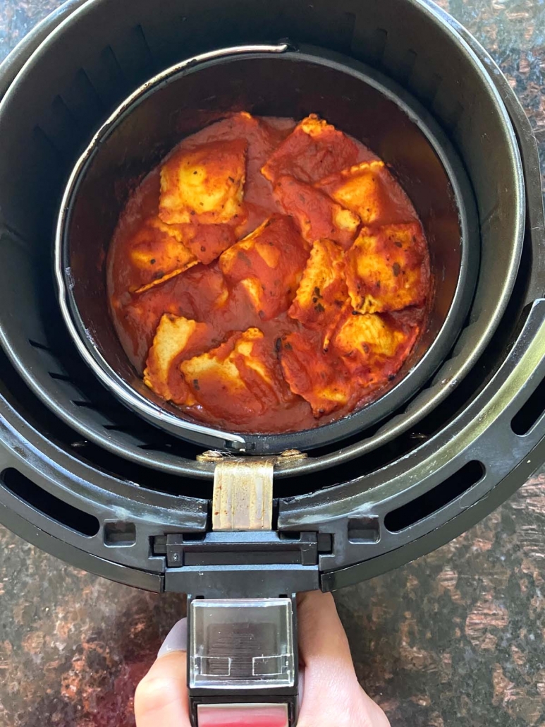 hand holding air fryer with baking pan filled with ravioli