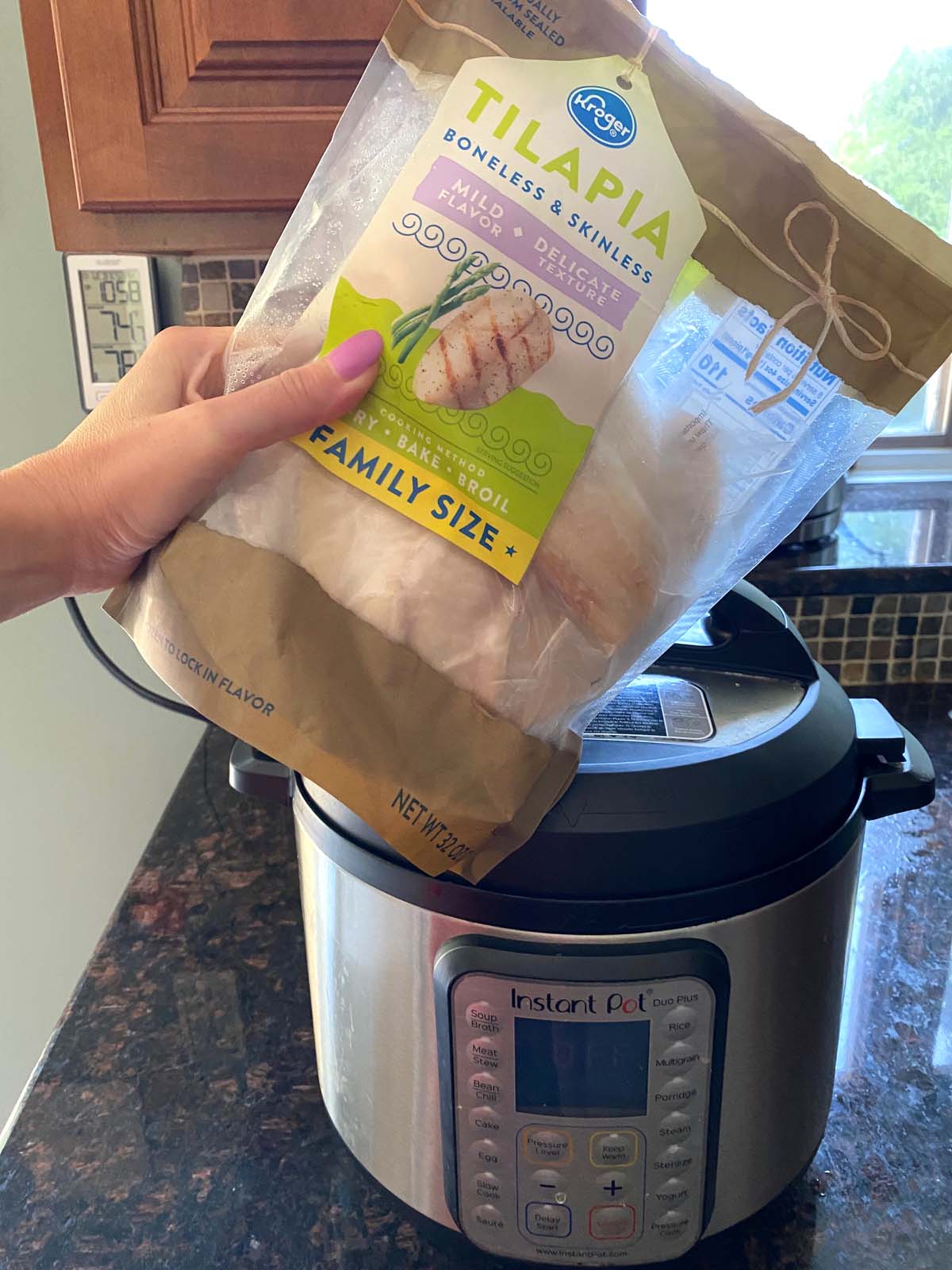 Hand holding a package of frozen tilapia infront of Instant pot.