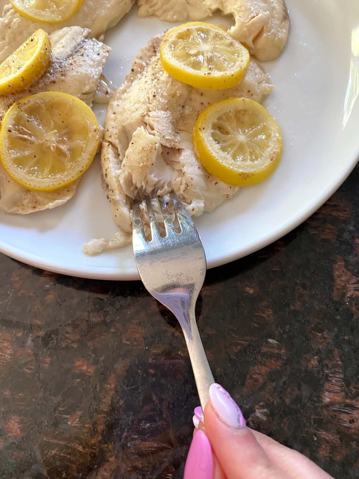 Fork flaking cooked fish garnished with lemon.