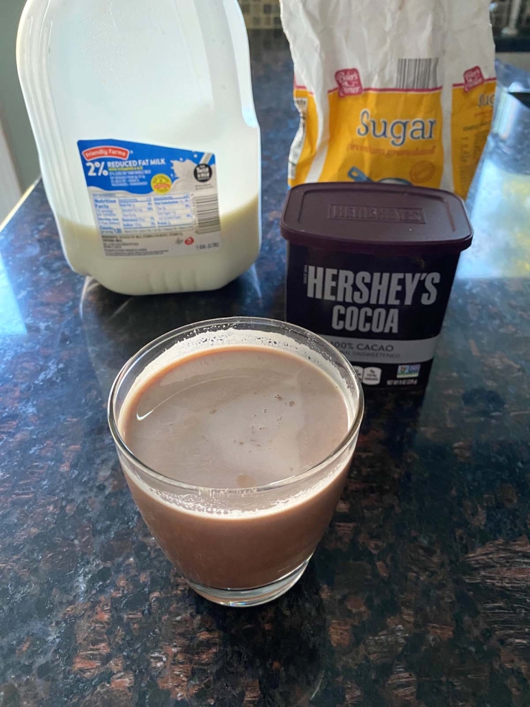 milk, sugar, and cocoa powder next to a glass of chocolate milk