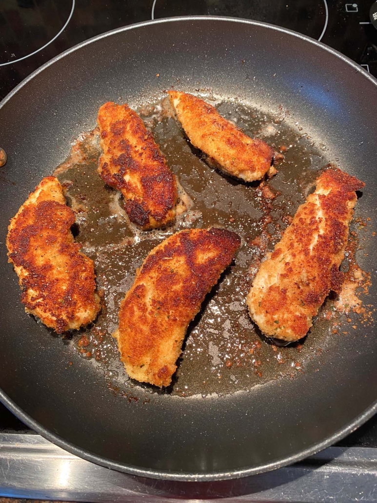 breaded chicken tenders pan frying in a skillet