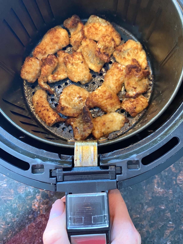 hand holding air fryer with breaded catfish nuggets