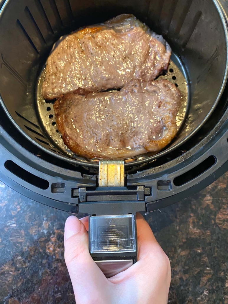 hand holding air fryer with seasoned steak inside