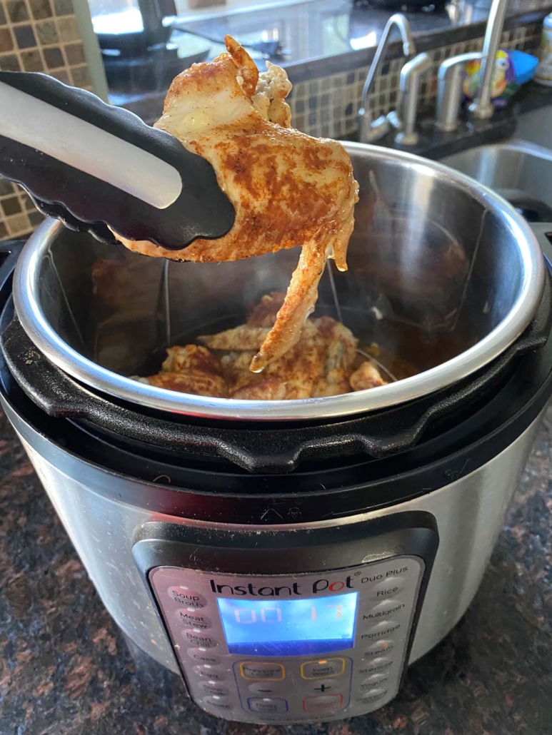 tongs pulling a chicken wing out of an instant pot