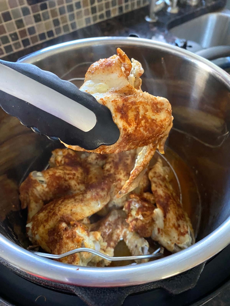 tongs holding a tender chicken wing cooked in the instant pot