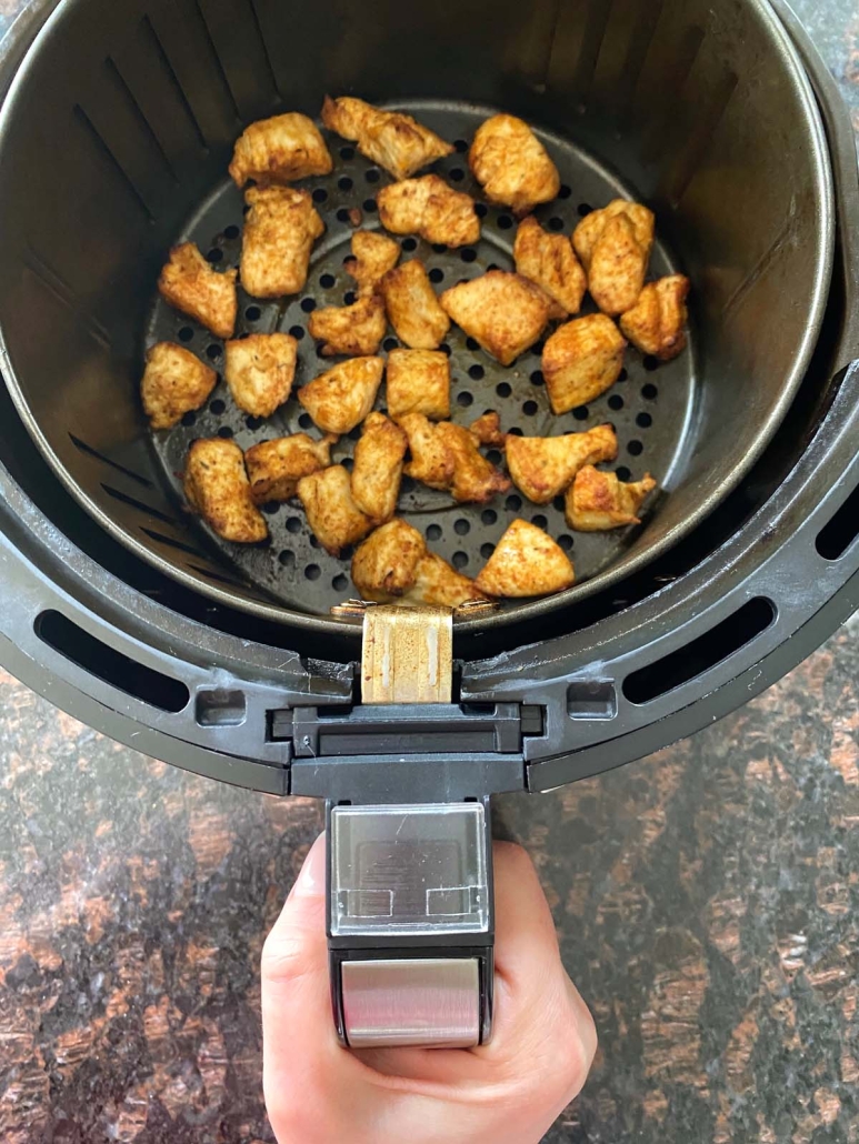 hand holding air fryer basket with seasoned chicken bites inside