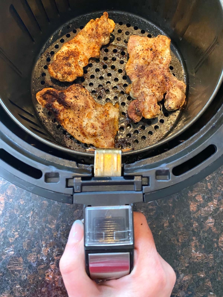 hand holding air fryer containing boneless skinless chicken thighs