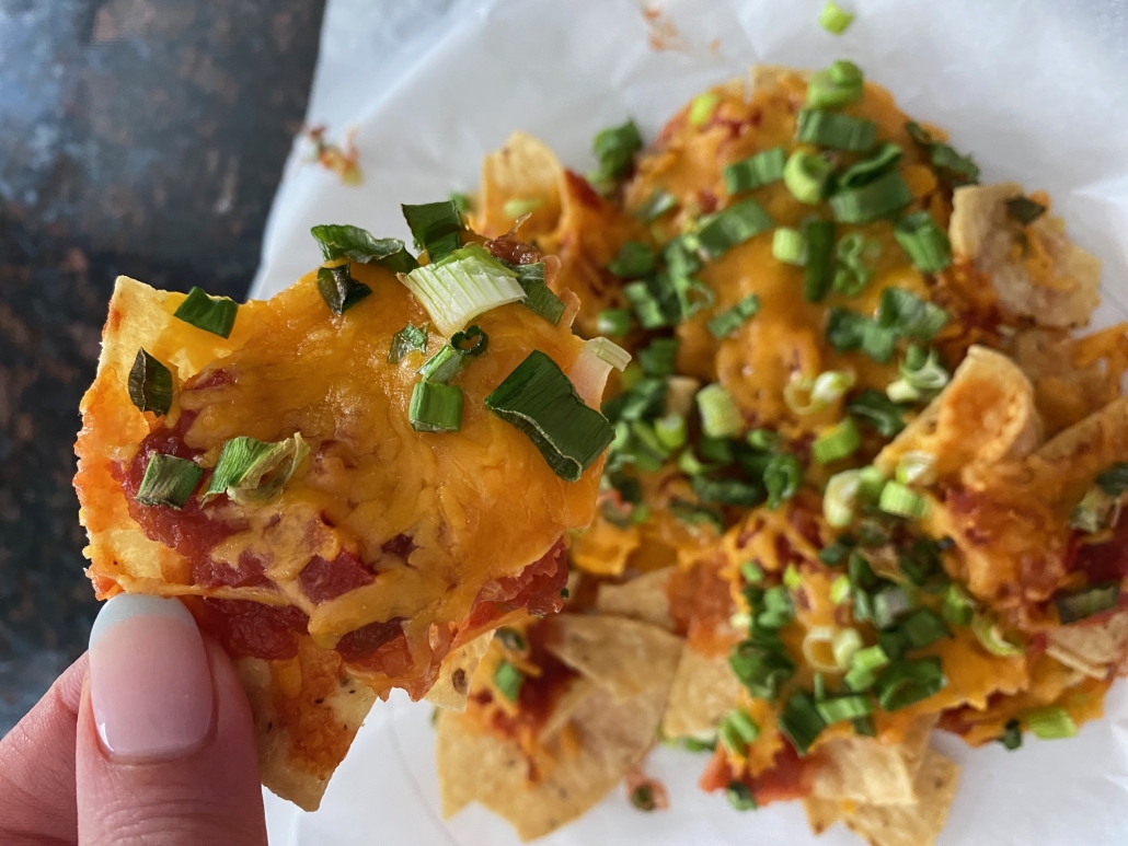 hand holding tortilla chip with nacho ingredients on top