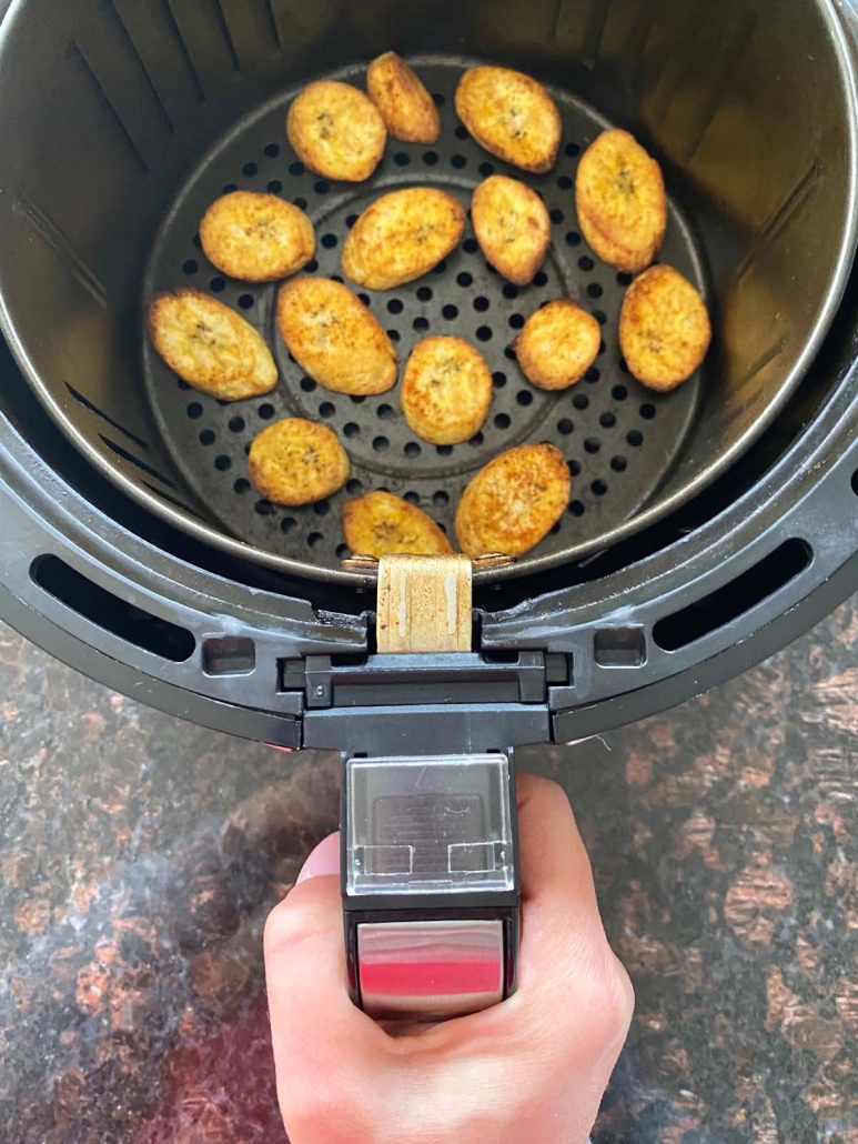 hand holding air fryer basket with sliced plantains inside