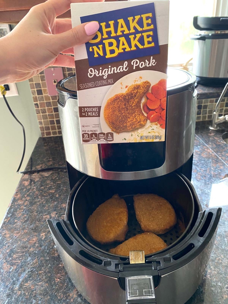 hand holding Shake N Bake mix above an air fryer with pork chops
