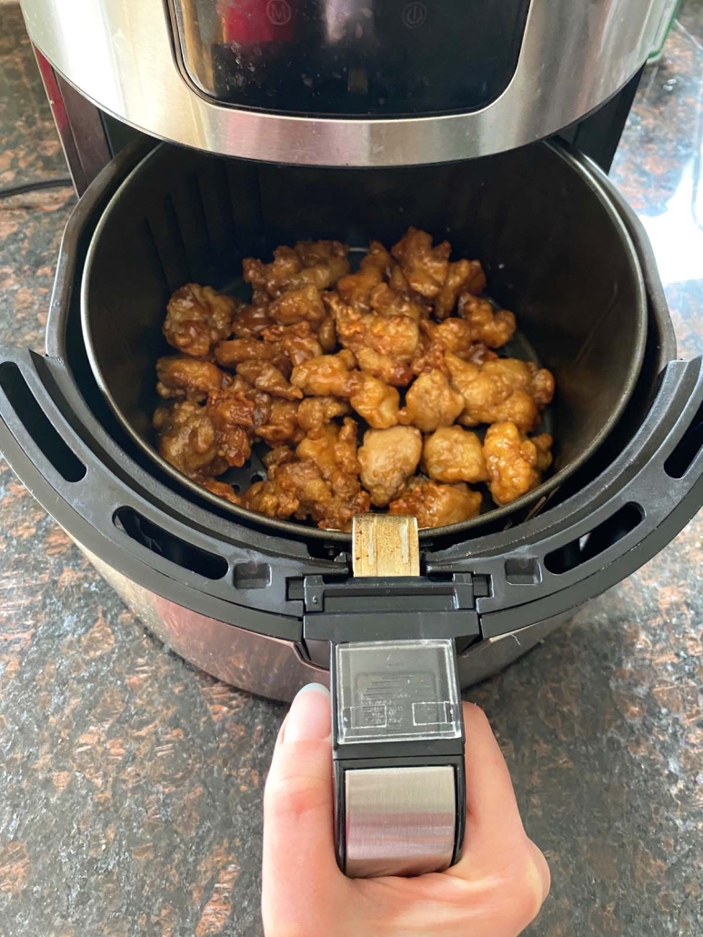 hand pulling out air fryer basket to show cooking Trader Joe’s Orange Chicken