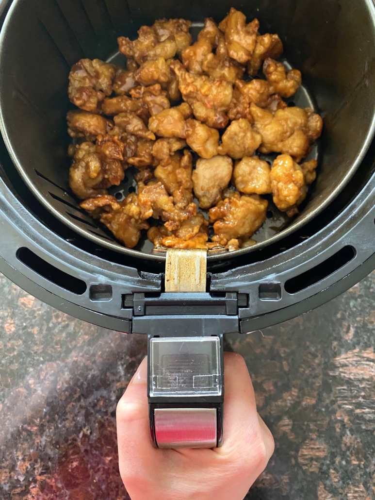 hand holding air fryer basket with Air Fryer Trader Joe’s Orange Chicken inside