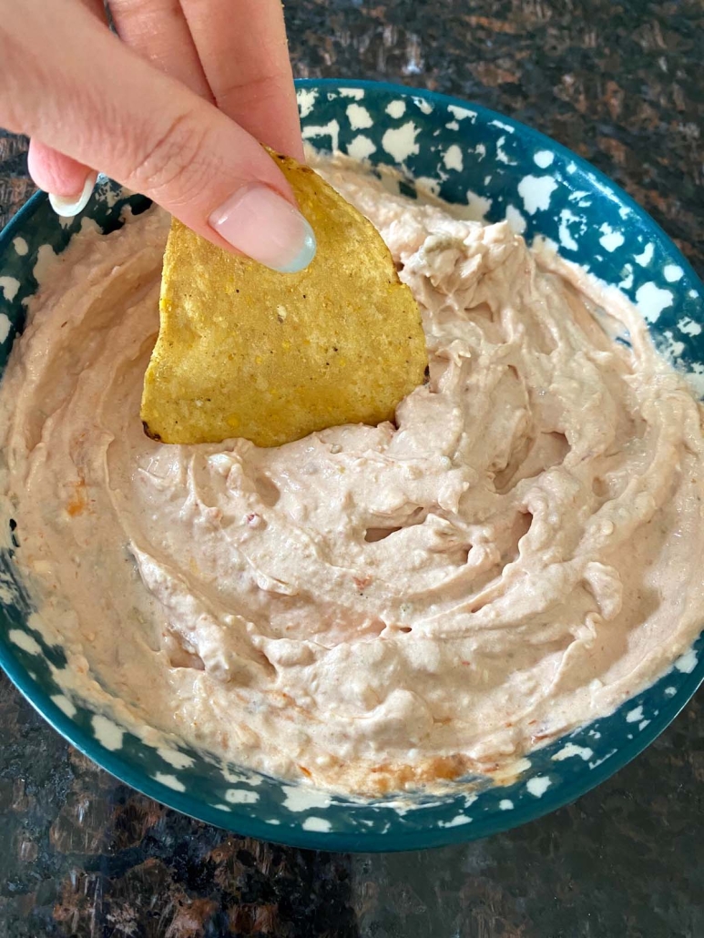 hand holding tortilla chip scooping up Cream Cheese And Salsa Dip