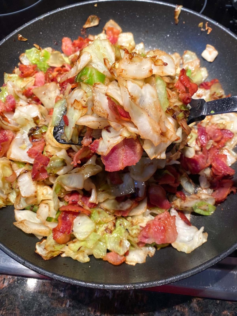 stirring up Fried Cabbage With Bacon in a skillet