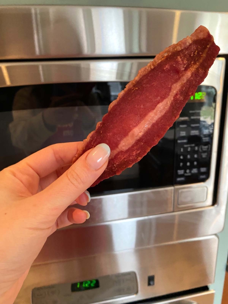 hand holding slice of turkey bacon in front of microwave